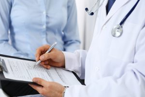 Male doctor holding application form while consulting female patient in hospital. Medicine and healthcare concept Male doctor holding application form while consulting female patient in hospital. Medicine and healthcare concept.