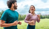 Multiethnic Friends Enjoying a Run in Urban Park A Middle Eastern male and Caucasian female jog together, sharing smiles in casual running gear, surrounded by lush greenery in a lively city park.